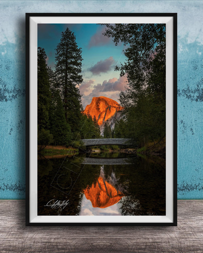 A framed photograph depicting a scenic landscape with a bridge, trees, and a mountain in the background, reflecting in a body of water.