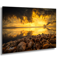 a serene landscape with a rocky shoreline, a calm body of water, and a dramatic sky filled with clouds and a vibrant sunset.