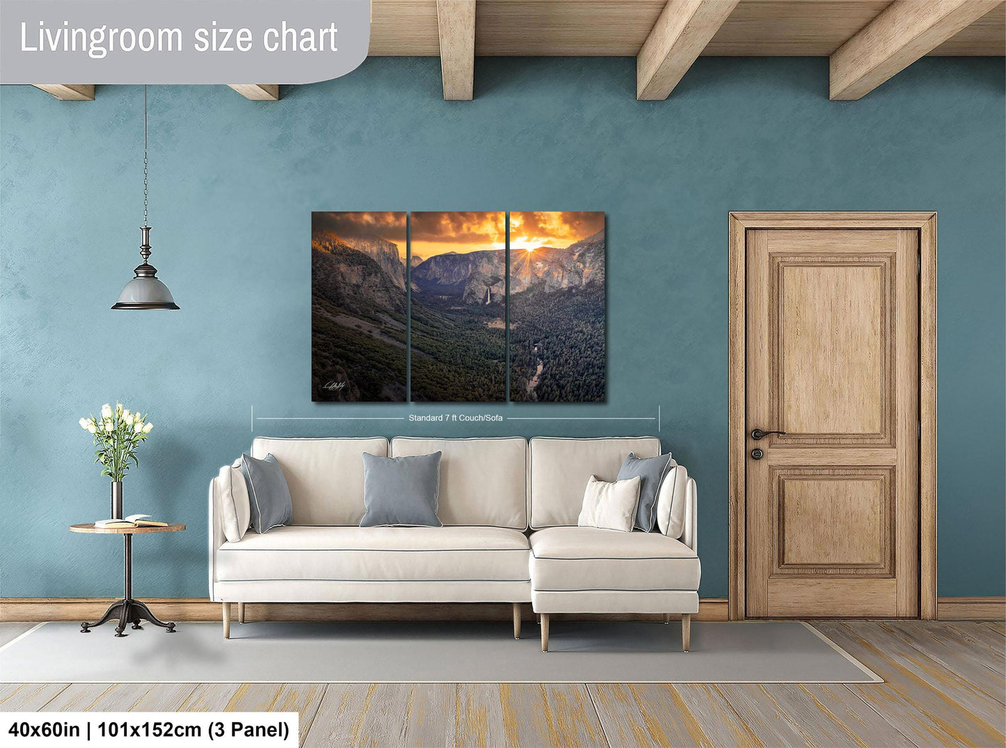 The image is a living room with a large, three-panel landscape painting hanging on the wall. The painting depicts a mountainous scene with a sunset in the background. The room has a white sofa and a wooden door, creating a cozy and inviting atmosphere.