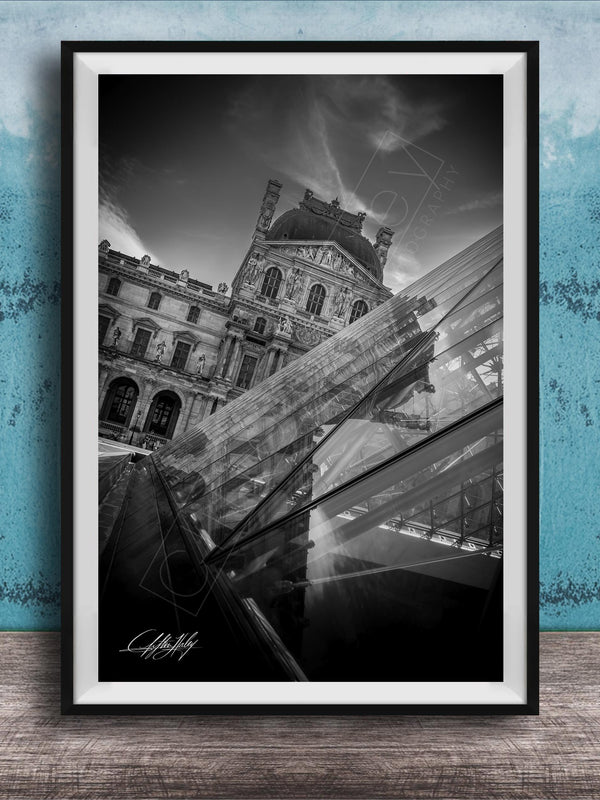 A black and white photograph of the Louvre Museum in Paris, France, with a modern glass structure in the foreground.