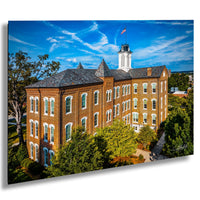 A large brick building with a clock tower, surrounded by trees and a blue sky with clouds.