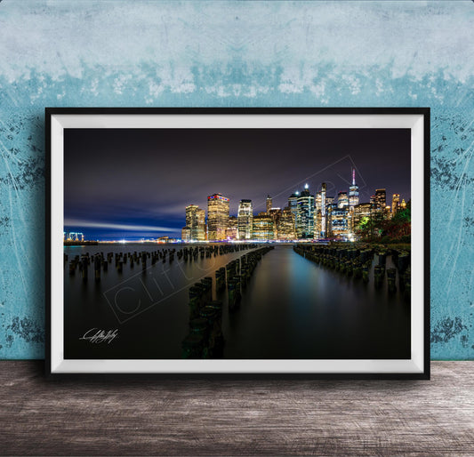 A framed photograph of the New York City skyline at night, with the city's iconic skyscrapers and landmarks illuminated against a dark sky.