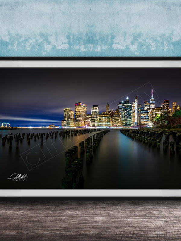 A framed photograph of the New York City skyline at night, with the city's iconic skyscrapers and landmarks illuminated against a dark sky.
