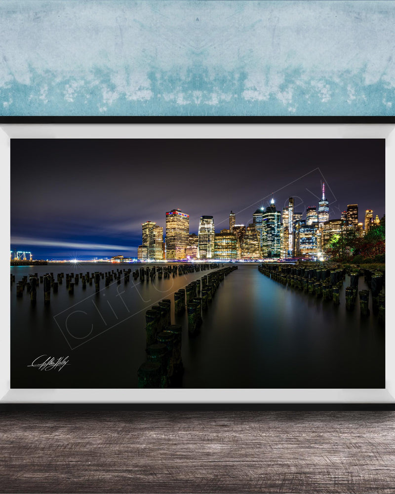 A framed photograph of the New York City skyline at night, with the city's iconic skyscrapers and landmarks illuminated against a dark sky.