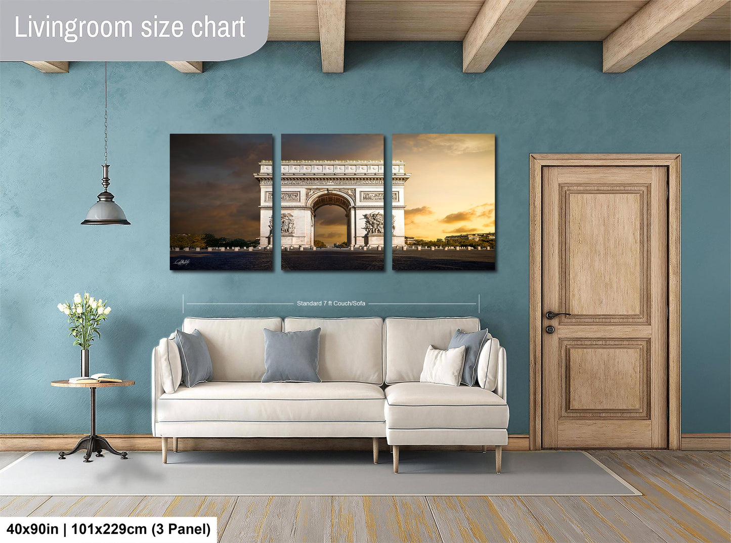 The image is a living room with a large white sofa and a wooden door. Above the sofa, there is a triptych of pictures depicting the Arc de Triomphe in Paris. The wall behind the sofa has a blue color, and there is a lamp hanging from the ceiling. The living room appears to be well-lit and spacious.