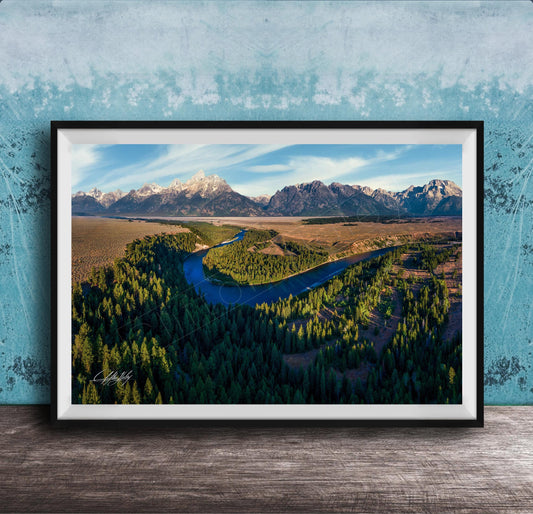 The image is a framed aerial view of a mountainous landscape with a winding river, surrounded by lush forests.