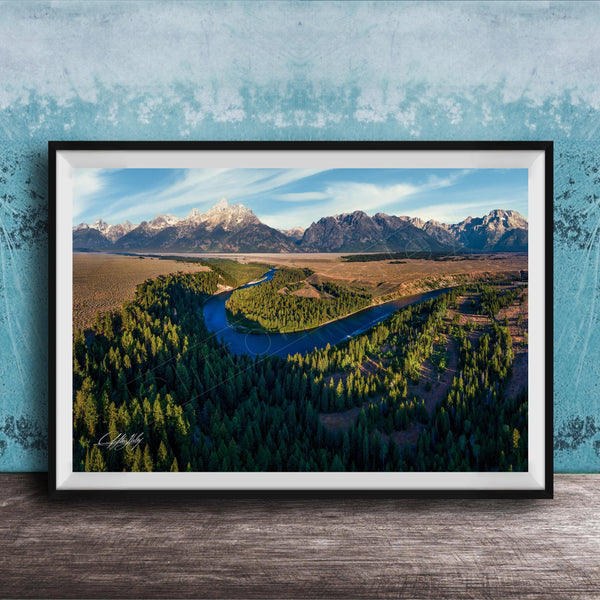 The image is a framed aerial view of a mountainous landscape with a winding river, surrounded by lush forests.