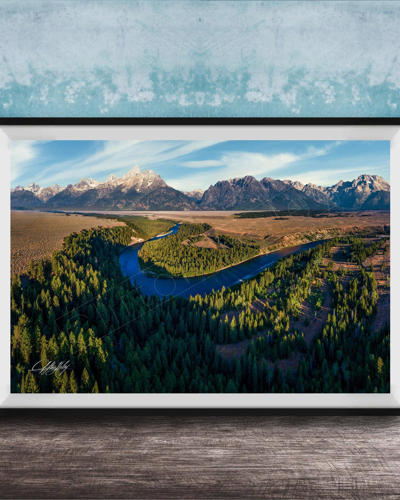 The image is a framed aerial view of a mountainous landscape with a winding river, surrounded by lush forests.