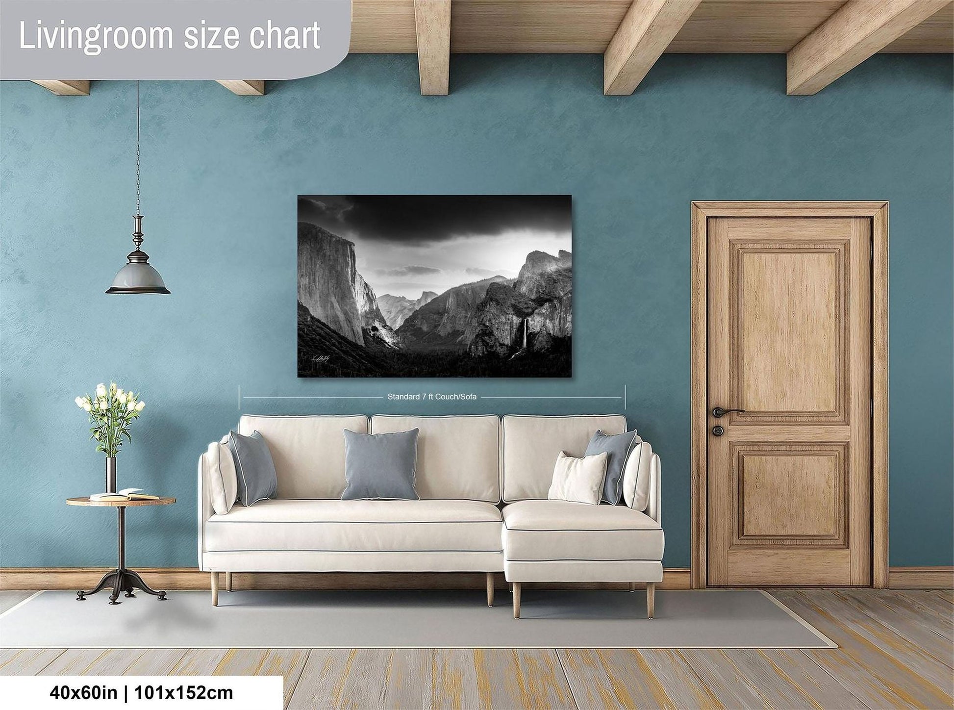 a living room with a large black and white photograph of a mountainous landscape hanging on the wall. The photograph is framed and measures 40 inches by 101.5 centimeters. The living room has a white sofa and a wooden door, creating a cozy and inviting atmosphere.