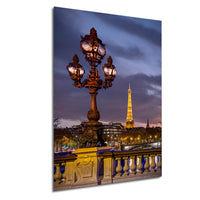 a large ornate street lamp with three lights, standing on a bridge with the Eiffel Tower visible in the background.