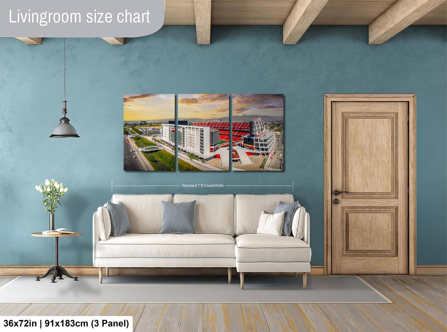 The image is a living room with a large white sofa and a wooden door. Above the sofa, there is a large wall art collage depicting a cityscape with buildings and a bridge. The collage is divided into three panels, with the largest panel covering the entire wall. The wall art is approximately 36 inches wide and 21 inches tall.