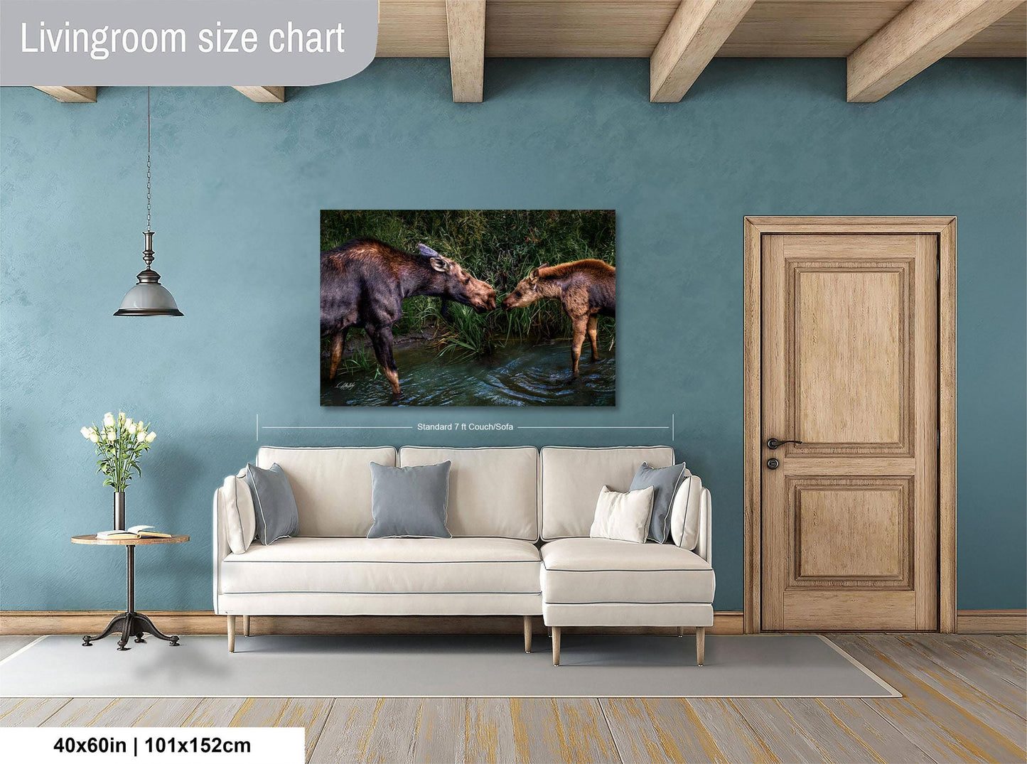 a living room with a large painting of two moose in a body of water hanging on the wall. The painting is framed and measures 40 inches by 101.5 centimeters. The room has a white sofa, a wooden door, and a small table with a vase of flowers.