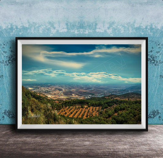The image is a framed photograph of a scenic landscape, featuring a valley with a city in the distance, surrounded by mountains and trees.