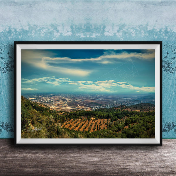 The image is a framed photograph of a scenic landscape, featuring a valley with a city in the distance, surrounded by mountains and trees.