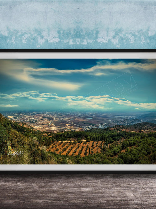 The image is a framed photograph of a scenic landscape, featuring a valley with a city in the distance, surrounded by mountains and trees.