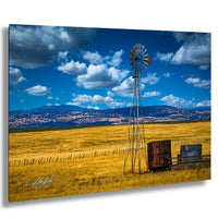 A windmill stands tall in a vast, golden field under a blue sky dotted with fluffy white clouds.
