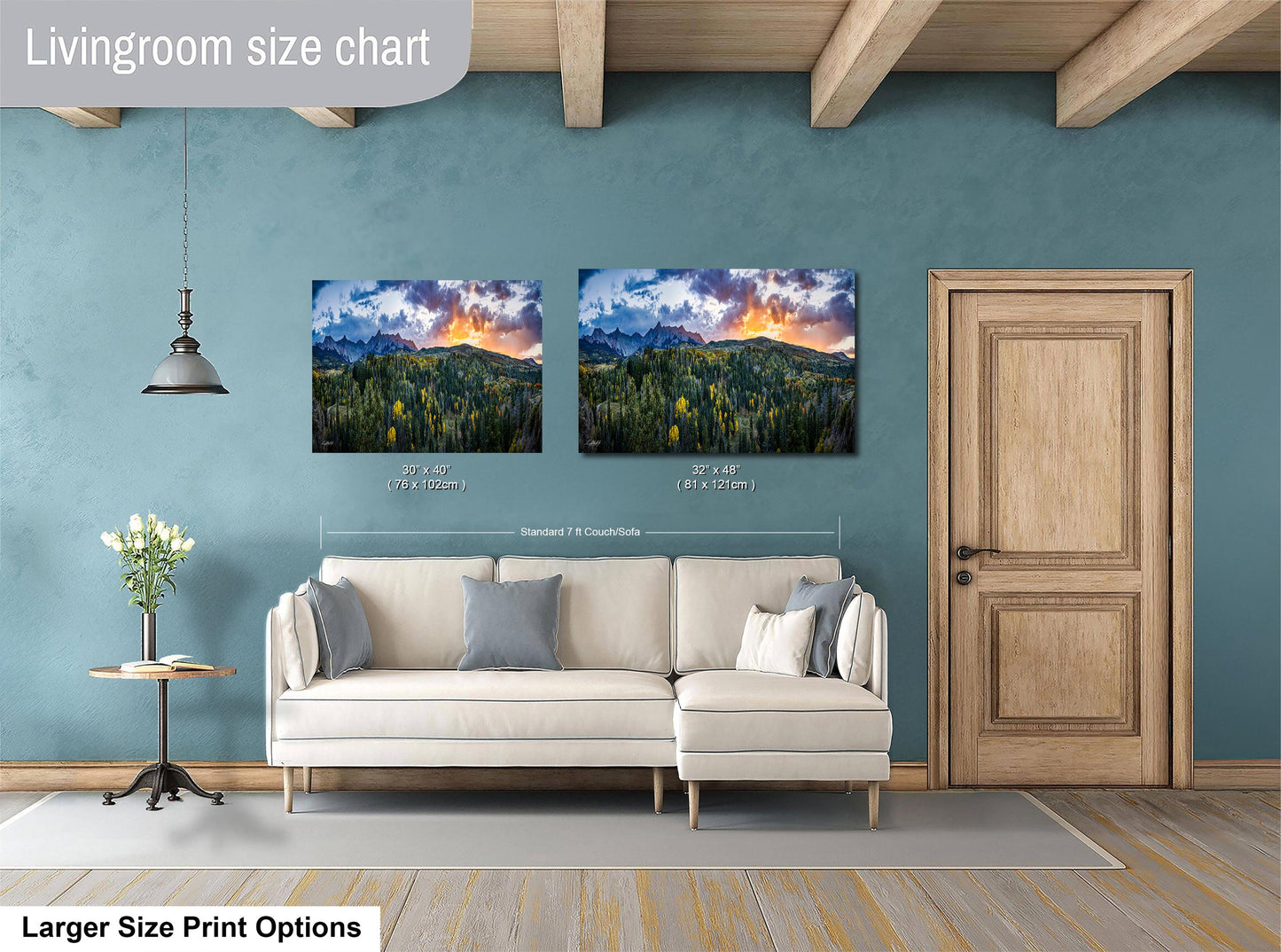 a living room with a white sofa and a wooden door. Above the sofa, there are two framed landscape paintings depicting a mountainous, forested scene with a sunset. The paintings are of similar size and style, suggesting they are intended to be hung together as a cohesive display.