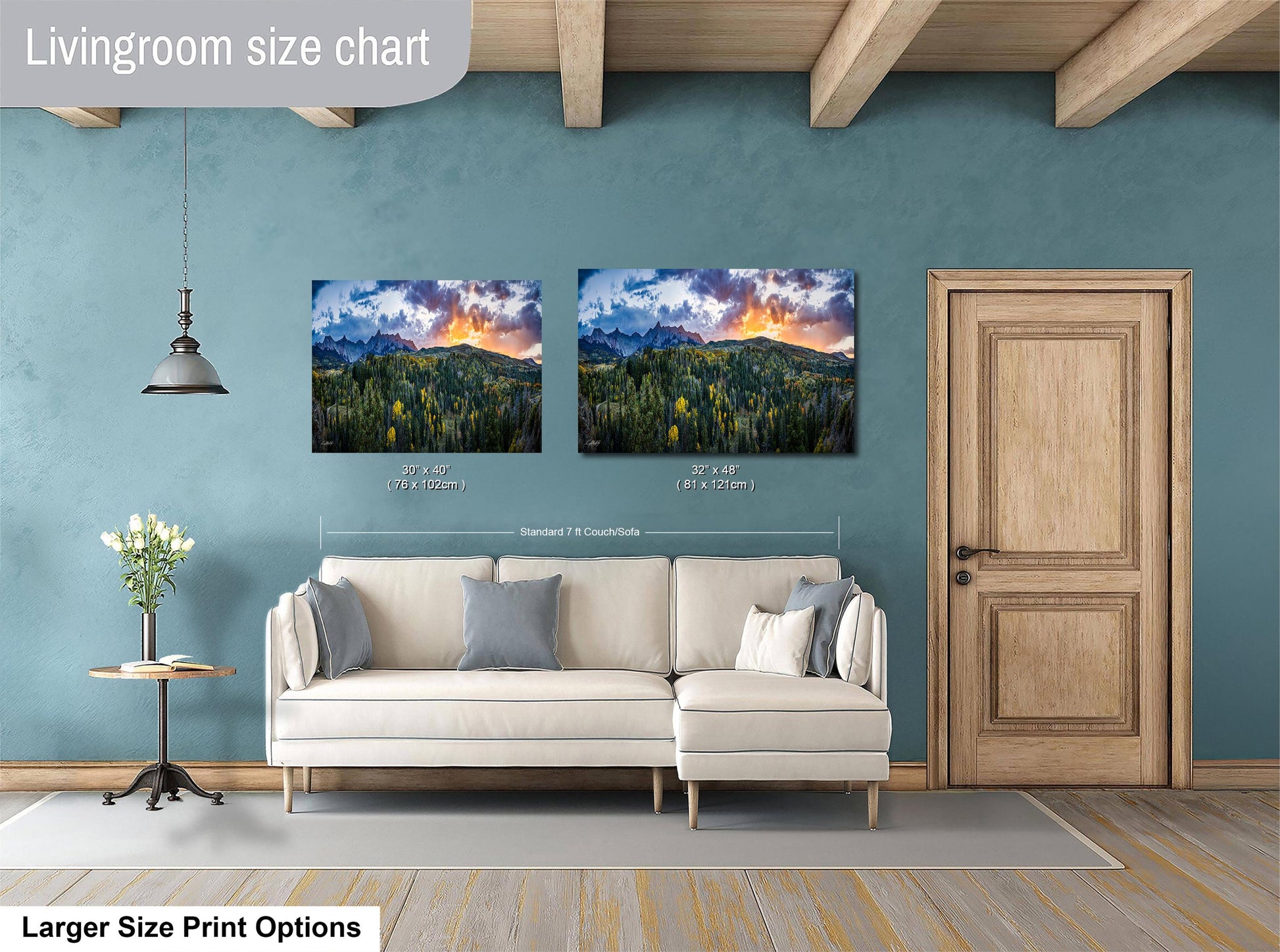 a living room with a white sofa and a wooden door. Above the sofa, there are two framed landscape paintings depicting a mountainous, forested scene with a sunset. The paintings are of similar size and style, suggesting they are intended to be hung together as a cohesive display.