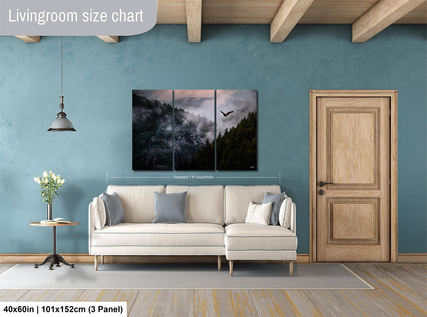 The image is a living room with a large white sofa, a wooden door, and a painting of a forest scene above it. The painting is a triptych, with the top and bottom panels depicting a mountain landscape with a bird in flight. The wall behind the sofa is painted a light blue color, and there is a wooden table with a vase of flowers on it. The image is described as a living room size chart, indicating that it is a scale model or a representation of the actual room.