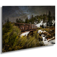 A wooden bridge spans a snowy, forested landscape under a starry night sky.