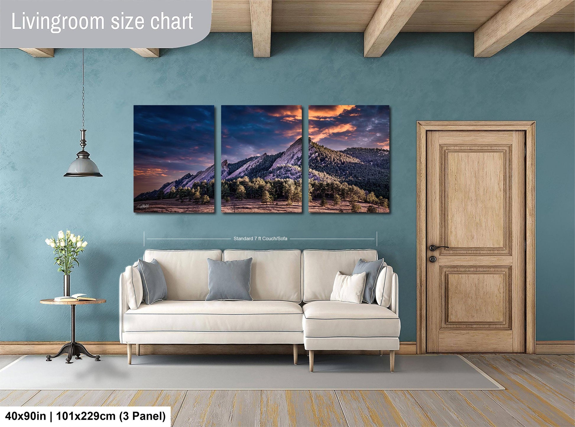 The image is a living room with a large wall art depicting a mountain landscape at sunset. The wall art is divided into three panels, each showing a different part of the mountain and sky. The room has a white sofa, a wooden door, and a small table with a vase of flowers. The living room size chart indicates that the wall art is approximately 40 inches wide and 101.29 cm tall, with a 3-panel layout.