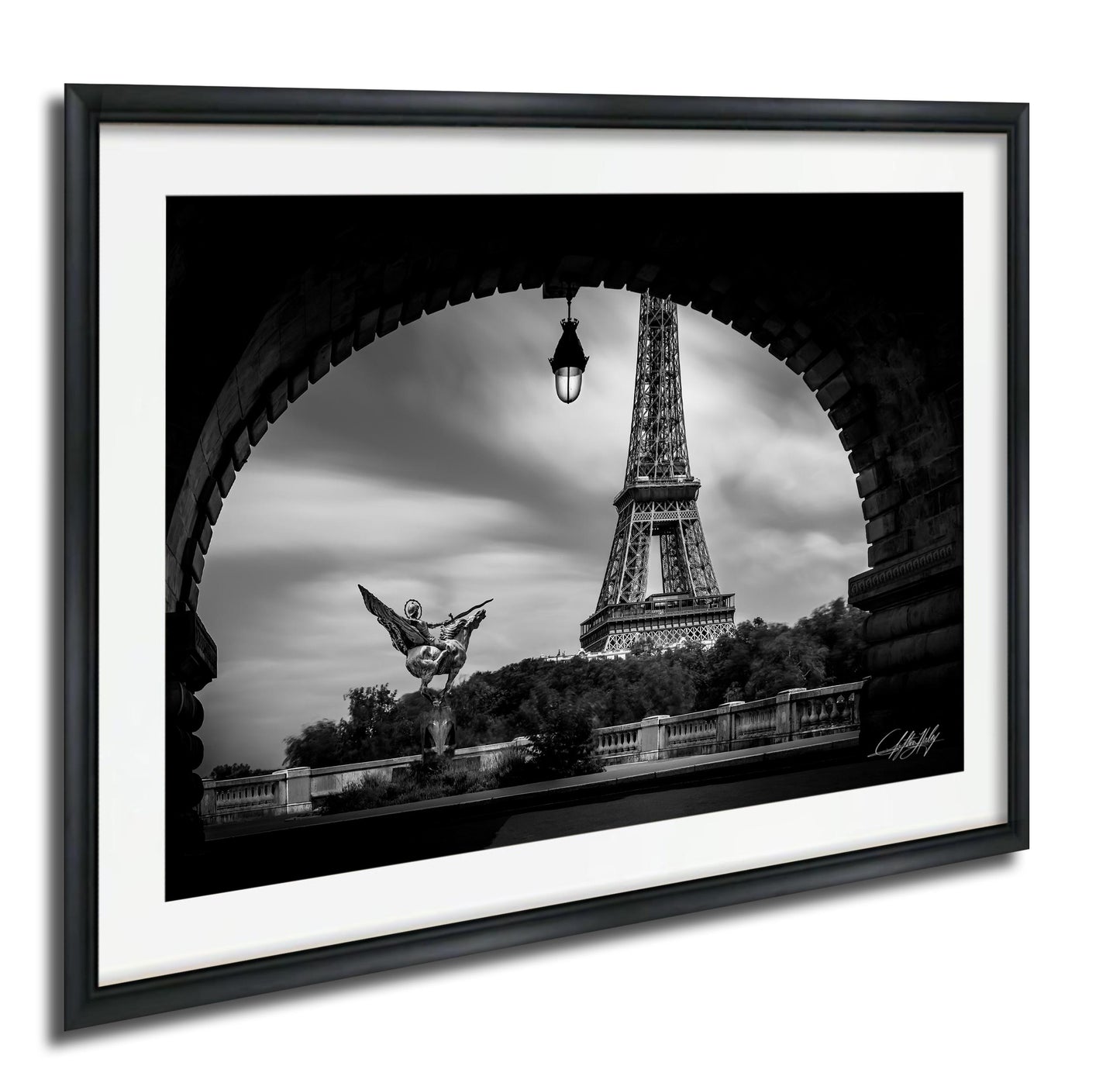 A black and white photograph of the Eiffel Tower in Paris, France, framed in a black frame and displayed on a wall.