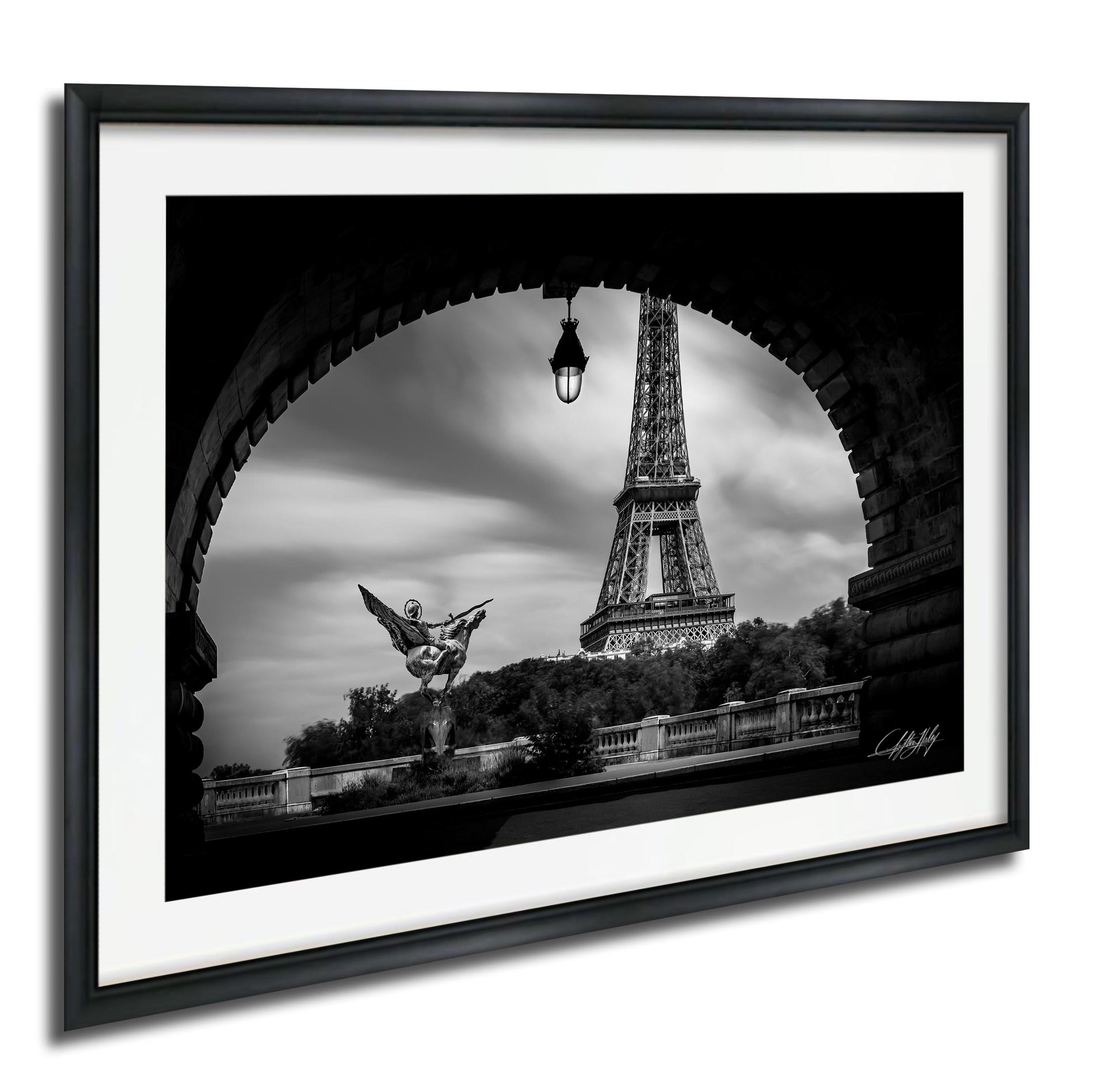A black and white photograph of the Eiffel Tower in Paris, France, framed in a black frame and displayed on a wall.