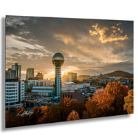 a city skyline at sunset, with a large tower in the center and a mix of modern and older buildings surrounding it. The sky is filled with clouds and the sun is setting, casting a warm glow over the scene.