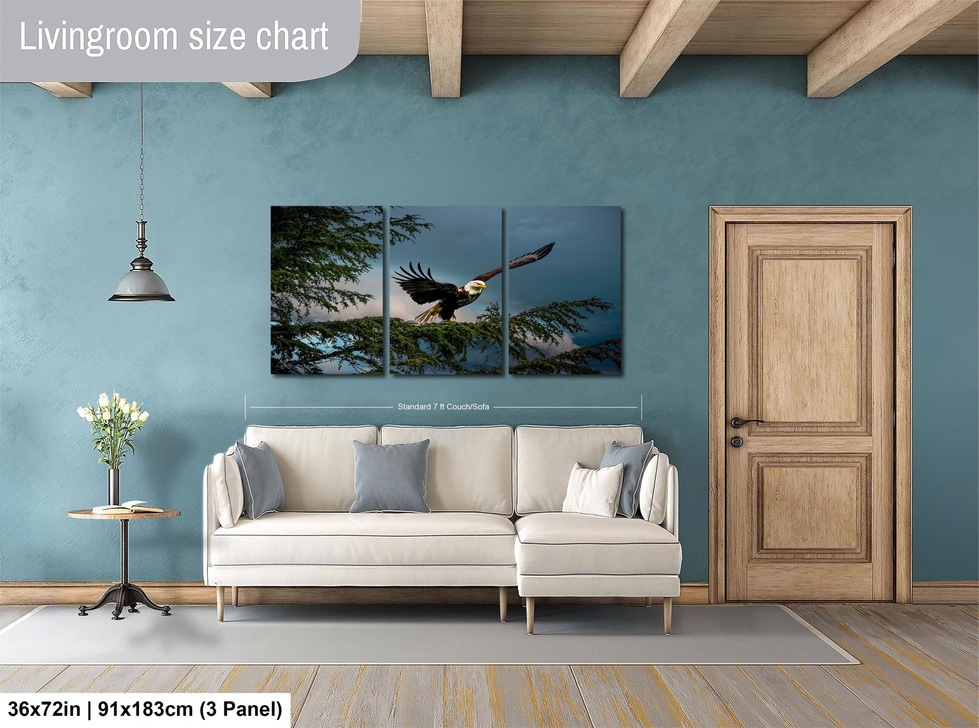 The image is a living room with a large white sofa, a wooden door, and a painting of a bald eagle in flight. The painting is divided into three panels, and the wall behind the sofa has a blue color.