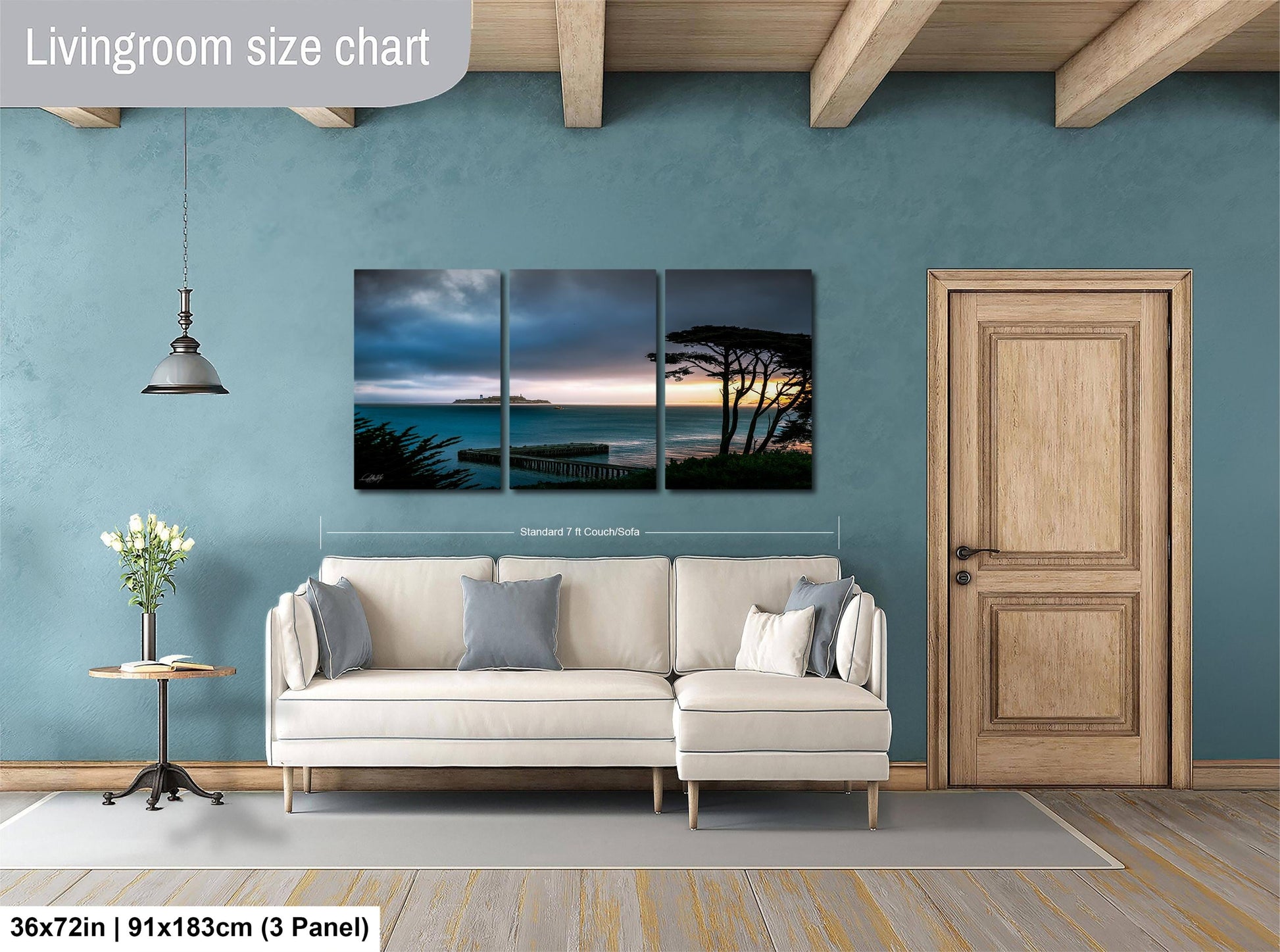 The image is a living room with a large wall art depicting a serene beach scene with a sunset. The living room has a white sofa and a wooden door, and the wall art is approximately 36 inches wide and 91 inches tall.