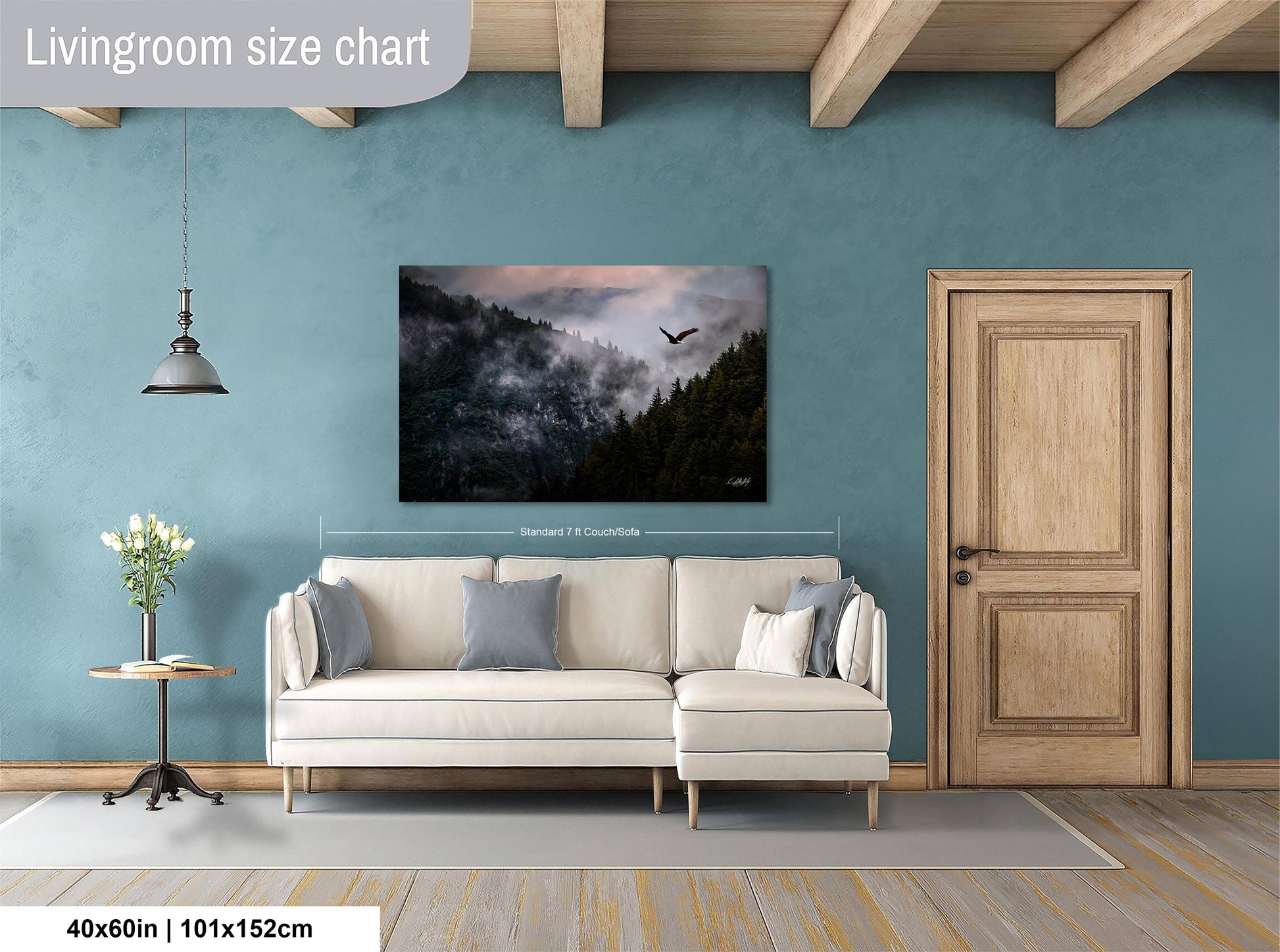 a living room with a large painting of a forest scene hanging on the wall. The painting is framed in a standard size of 70 centimeters by 150 centimeters. The room has a white sofa, a wooden door, and a wooden table with a vase of flowers.