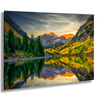 a serene mountain landscape with a calm lake reflecting the vibrant colors of the autumn foliage. The mountains are adorned with a mix of green and orange hues, creating a stunning natural scene. The sky above is a clear blue, providing a beautiful backdrop to the picturesque landscape. The image is a captivating representation of the beauty of nature, showcasing the harmonious blend of colors and the tranquility of the surroundings.