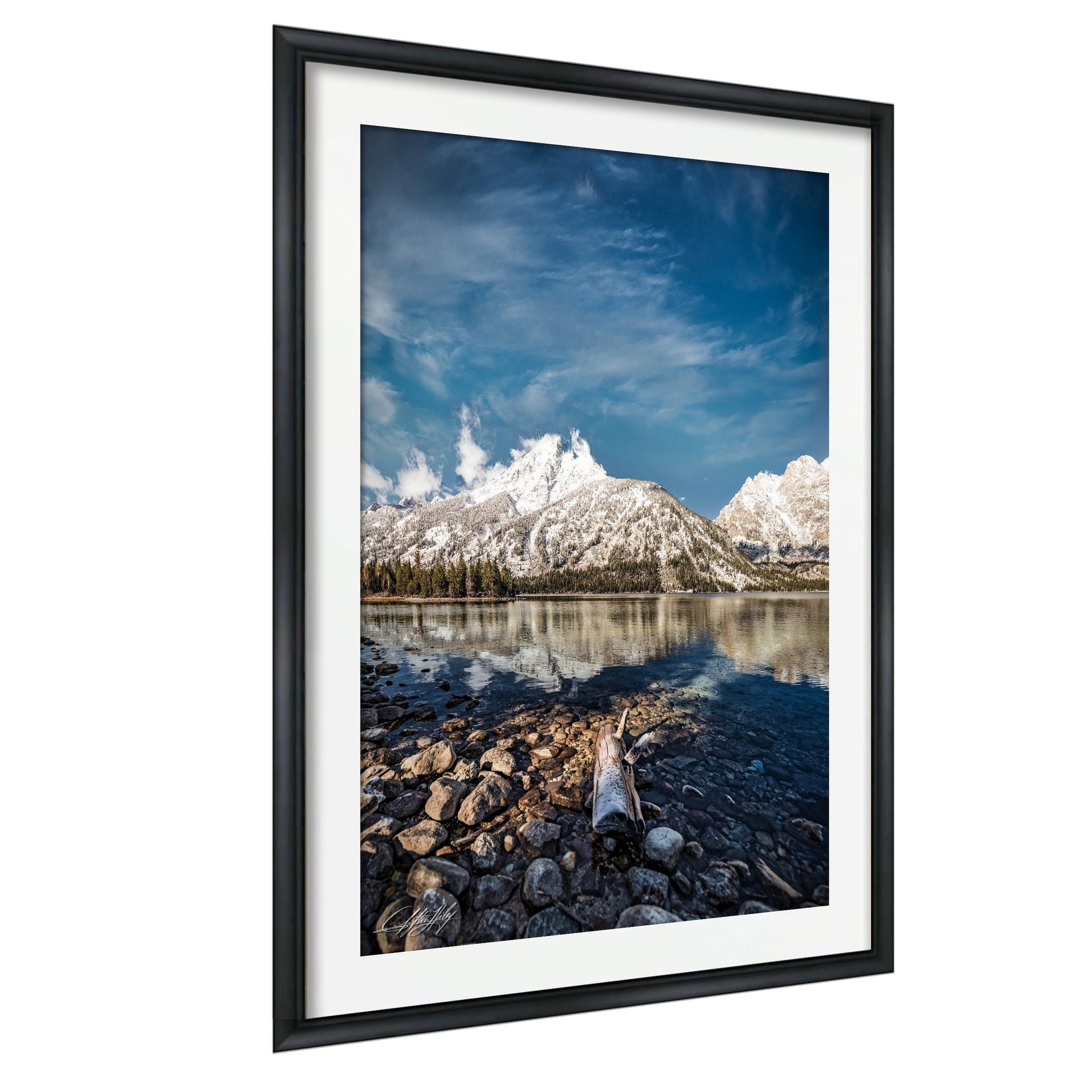 A framed photograph depicting a serene mountain landscape with a calm lake in the foreground, surrounded by snow-capped peaks and a clear blue sky.
