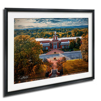 a large, red brick building with a clock tower, surrounded by trees with autumn foliage.