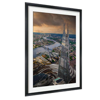The image is a framed aerial view of a cityscape, featuring a tall skyscraper, a river, and other buildings.
