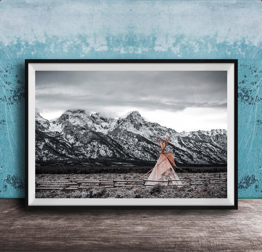A framed photograph of a teepee in a snowy mountain landscape, with a blue wall in the background.