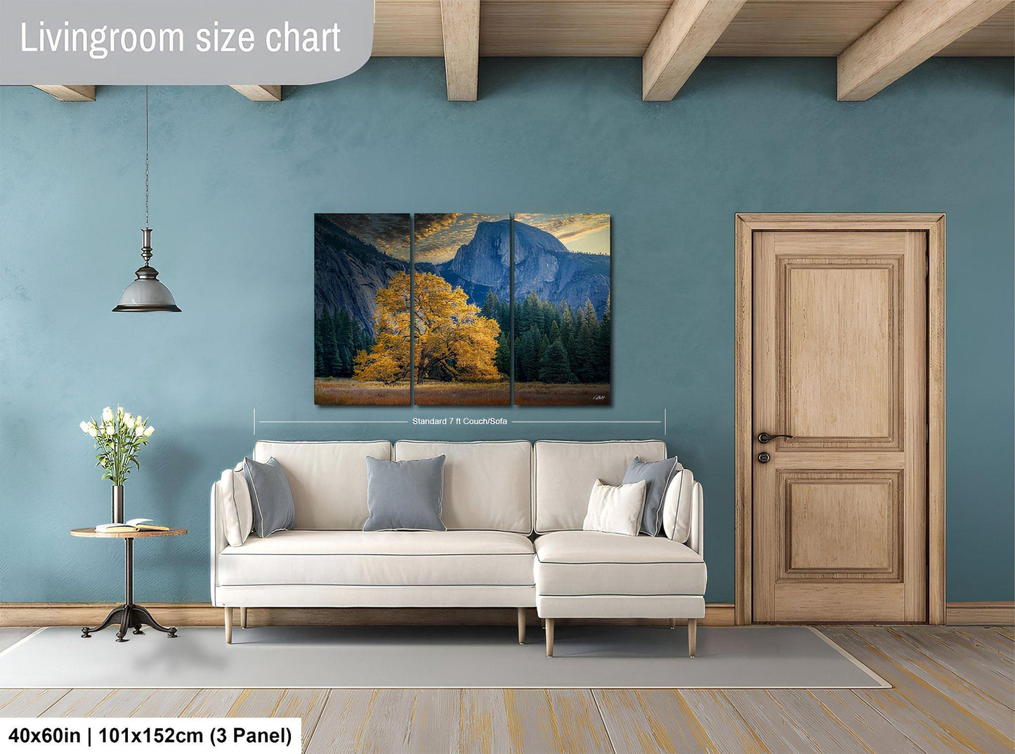 The image is a living room with a large painting of a mountain landscape hanging on the wall. The painting is divided into three panels, and the living room has a white sofa, a wooden door, and a small table with a vase of flowers.