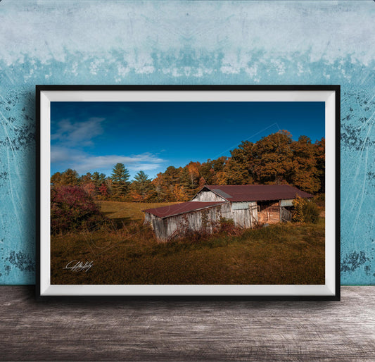 a rustic wooden barn nestled in a lush, green landscape with trees displaying autumn colors.