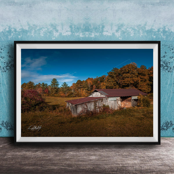 a rustic wooden barn nestled in a lush, green landscape with trees displaying autumn colors.