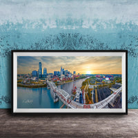 The image is a framed aerial view of a city skyline, featuring a bridge and a river.