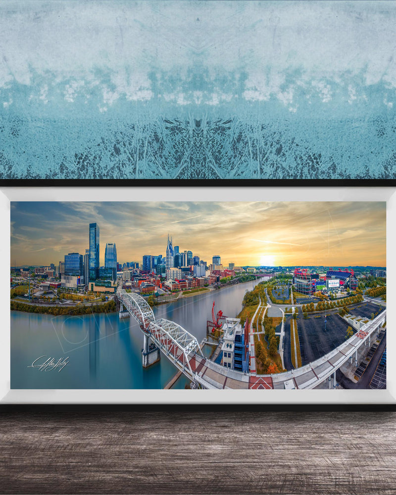 The image is a framed aerial view of a city skyline, featuring a bridge and a river.