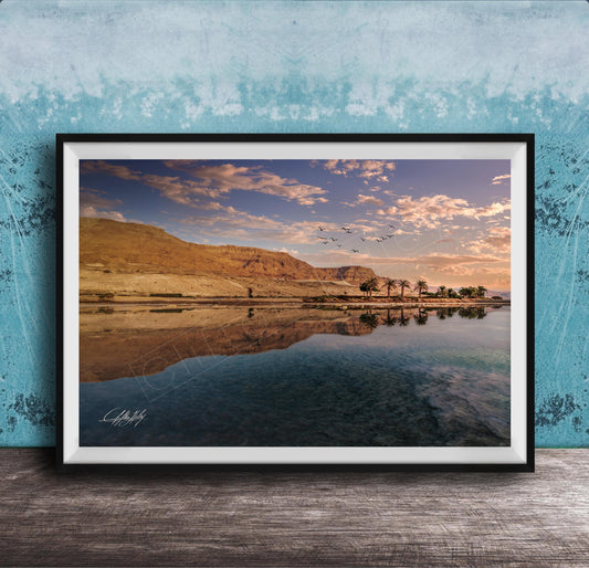 The image is a framed photograph depicting a serene landscape with a calm body of water reflecting the sky and mountains in the background.