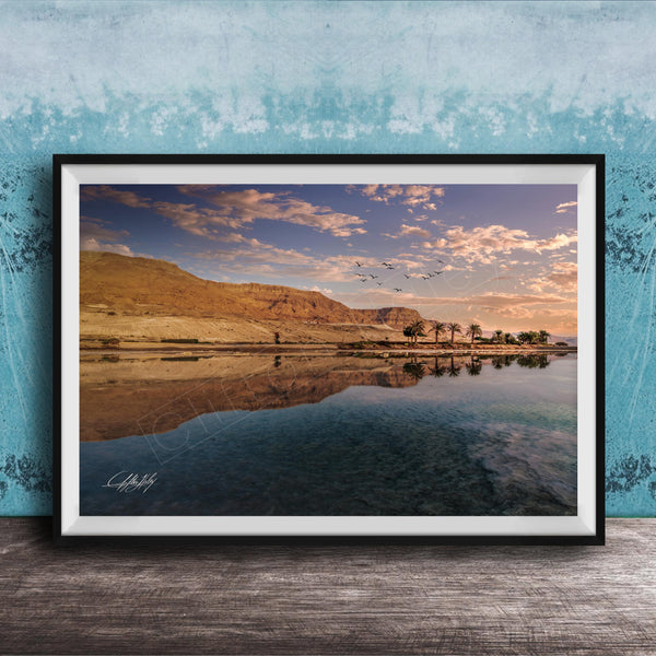 The image is a framed photograph depicting a serene landscape with a calm body of water reflecting the sky and mountains in the background.