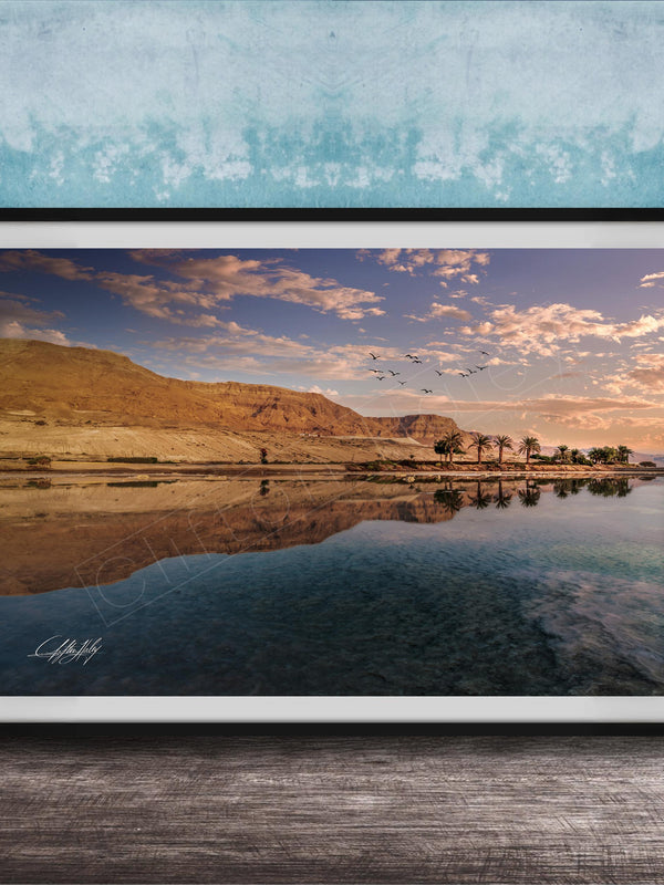The image is a framed photograph depicting a serene landscape with a calm body of water reflecting the sky and mountains in the background.