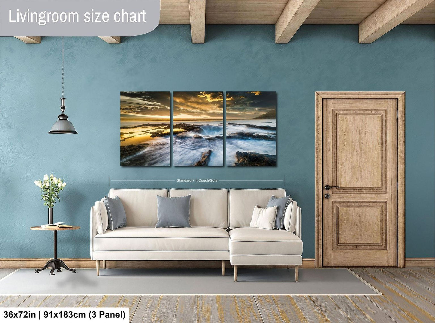 The image is a living room with a large painting of a beach scene hanging on the wall. The painting is divided into three panels, and the wall is painted a light blue color. There is a white sofa and a wooden door in the room.