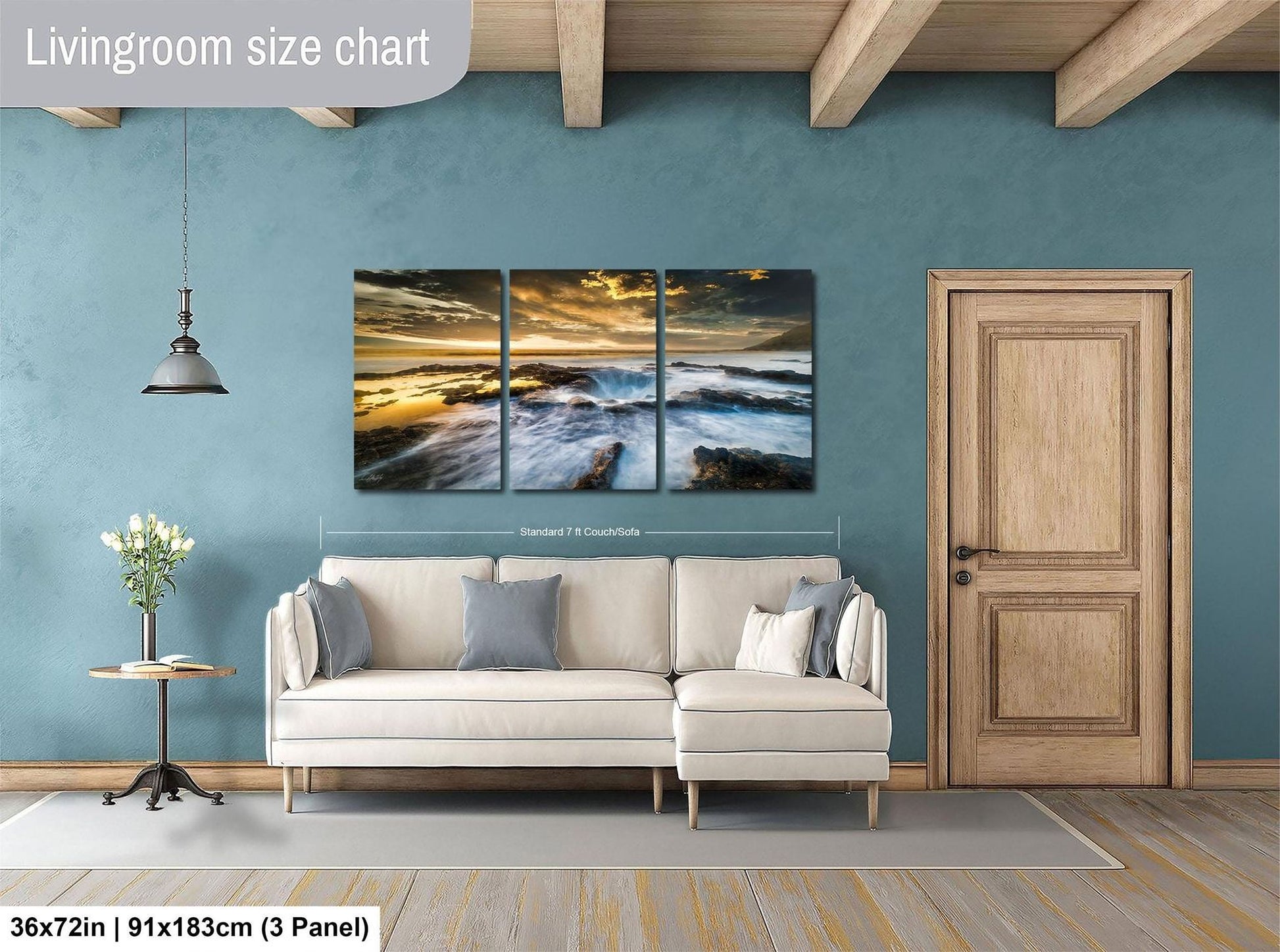The image is a living room with a large painting of a beach scene hanging on the wall. The painting is divided into three panels, and the wall is painted a light blue color. There is a white sofa and a wooden door in the room.