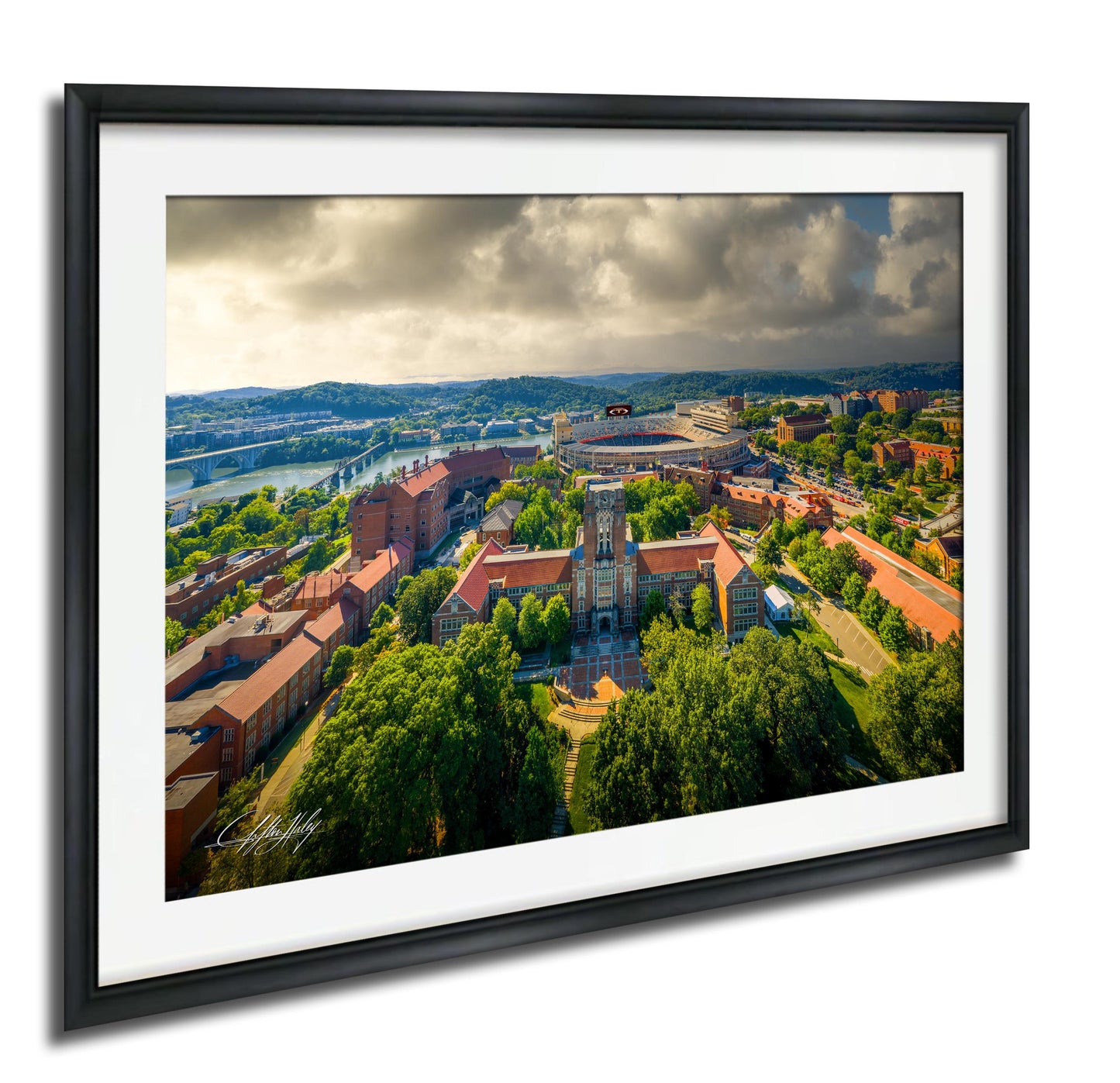 The image is a framed aerial view of a city with a mix of buildings, trees, and a river. The sky is cloudy, and the overall scene has a somewhat gloomy atmosphere.