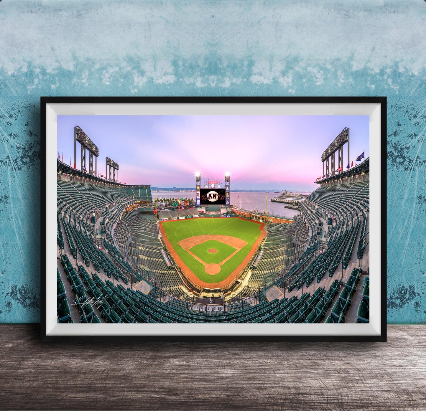 A framed photograph of a baseball stadium at dusk, with the field illuminated and the sky displaying a colorful sunset.