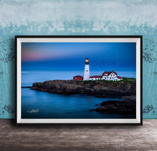 A framed photograph of a lighthouse on a rocky coastline, with the ocean and a colorful sky in the background.