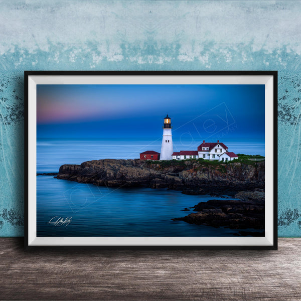 A framed photograph of a lighthouse on a rocky coastline, with the ocean and a colorful sky in the background.